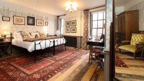 A traditional bedroom with a bed, a desk, and a chair. There are framed pictures on the wall and a chandelier above the bed. - Crown Hotel (Blandford Forum)