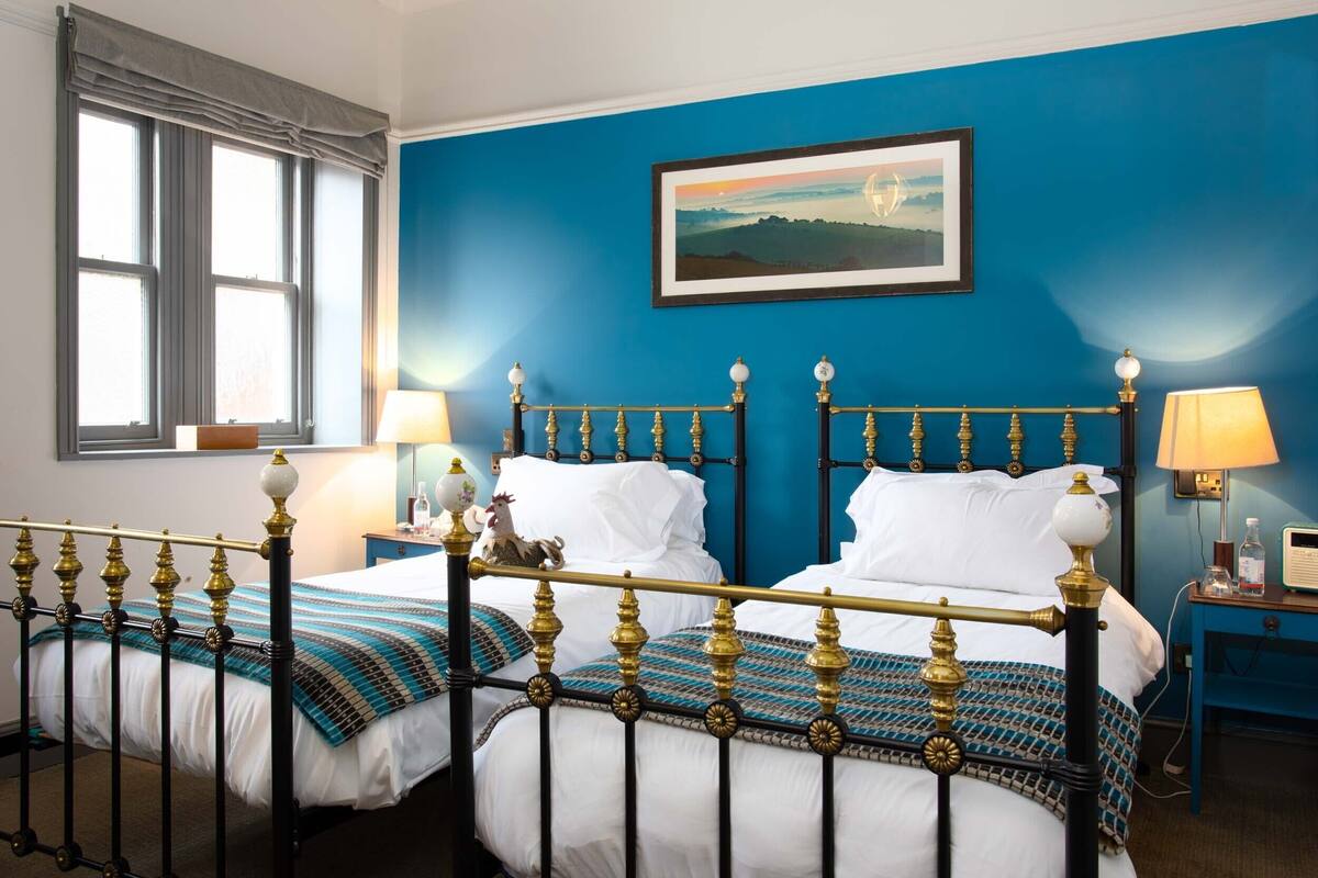 Ein Doppelbett mit schwarzem und goldenem Gestell, weißer Bettwäsche und einer blauen Wand mit einem gerahmten Bild darüber.