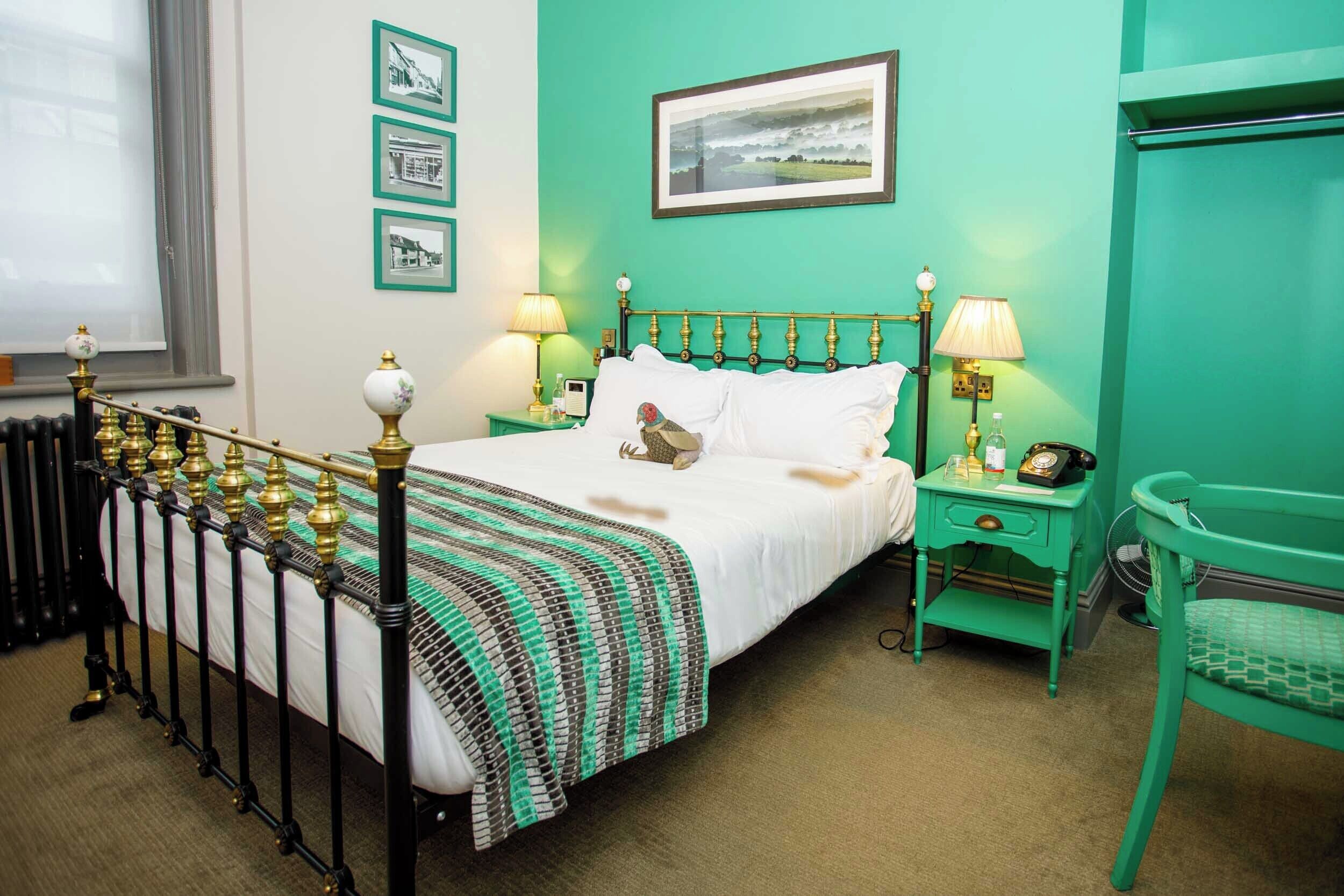 Una habitación con cama, paredes verdes, cuadros enmarcados, una ventana y una silla verde.