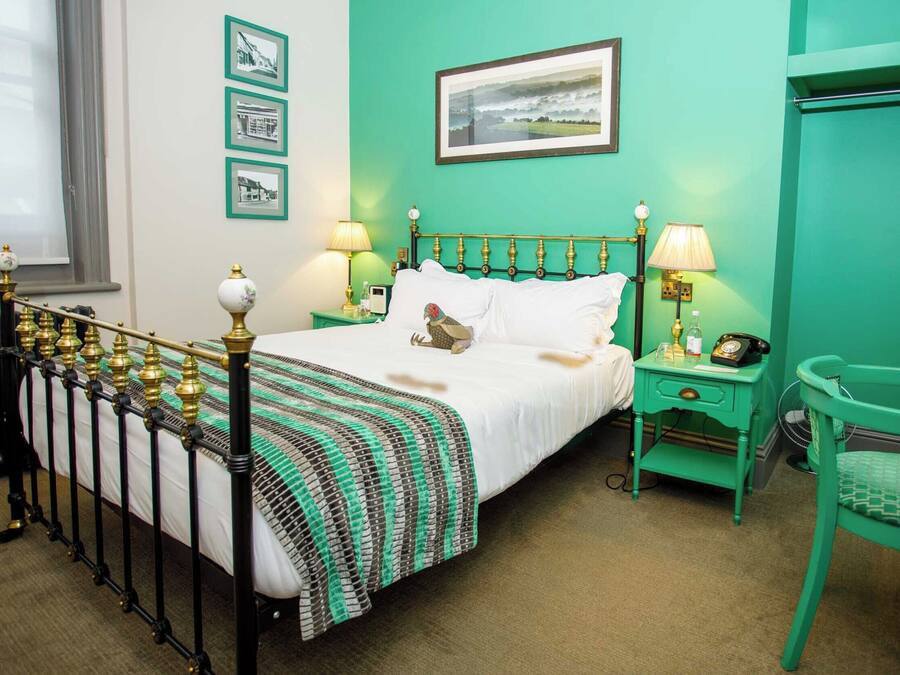 A room with a bed, green walls, framed pictures, a window, and a green chair.