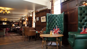A traditional room with wooden flooring, green upholstered chairs, a wooden table, and a bookshelf in the background. - Crown Hotel (Blandford Forum)