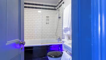 Un baño con pared de azulejos blancos, inodoro negro, bañera blanca y lavamanos blanco.