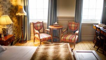 Une chambre d’hôtel avec un lit, deux fauteuils à carreaux, une petite table, une lampe et une fenêtre avec des rideaux.