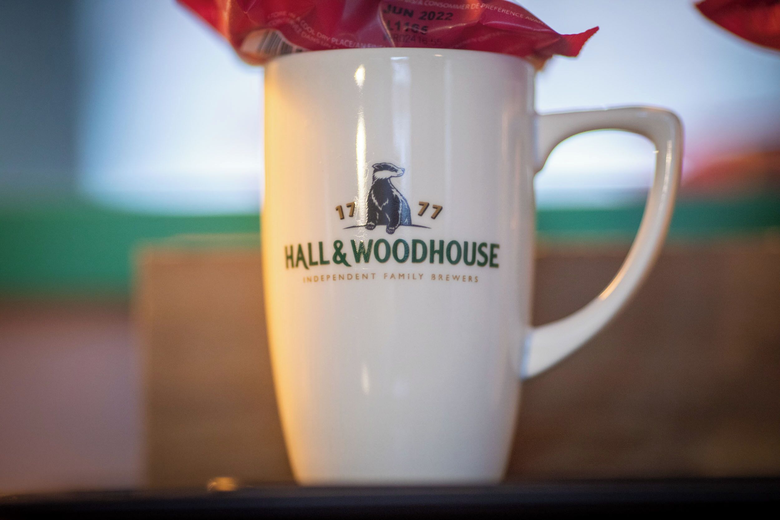 A white mug with the logo and text "Hall & Woodhouse Independent Family Brewers" on it.