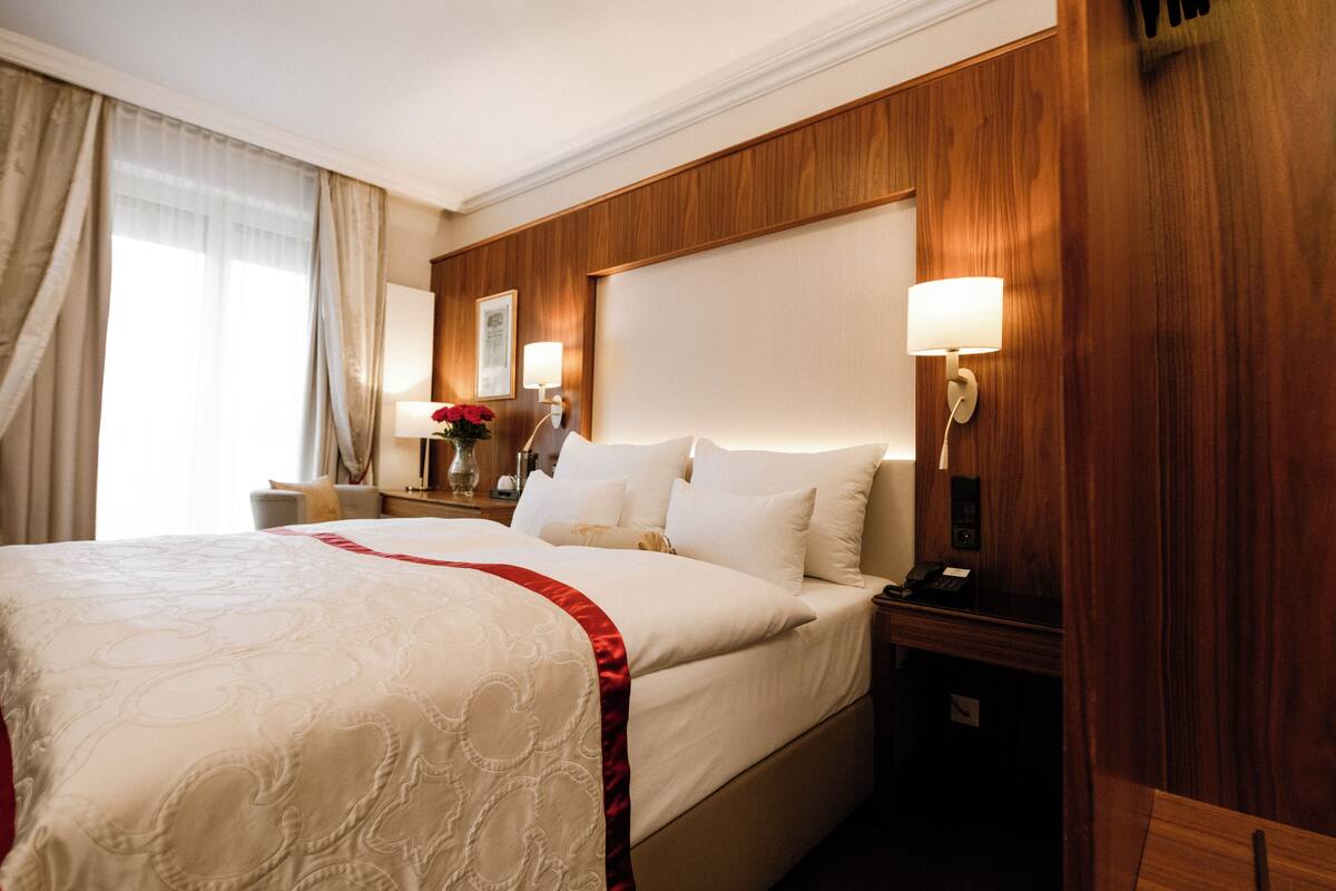 Een hotelkamer met een groot bed, een houten hoofdbord, bedlampjes en een nachtkastje met een telefoon.