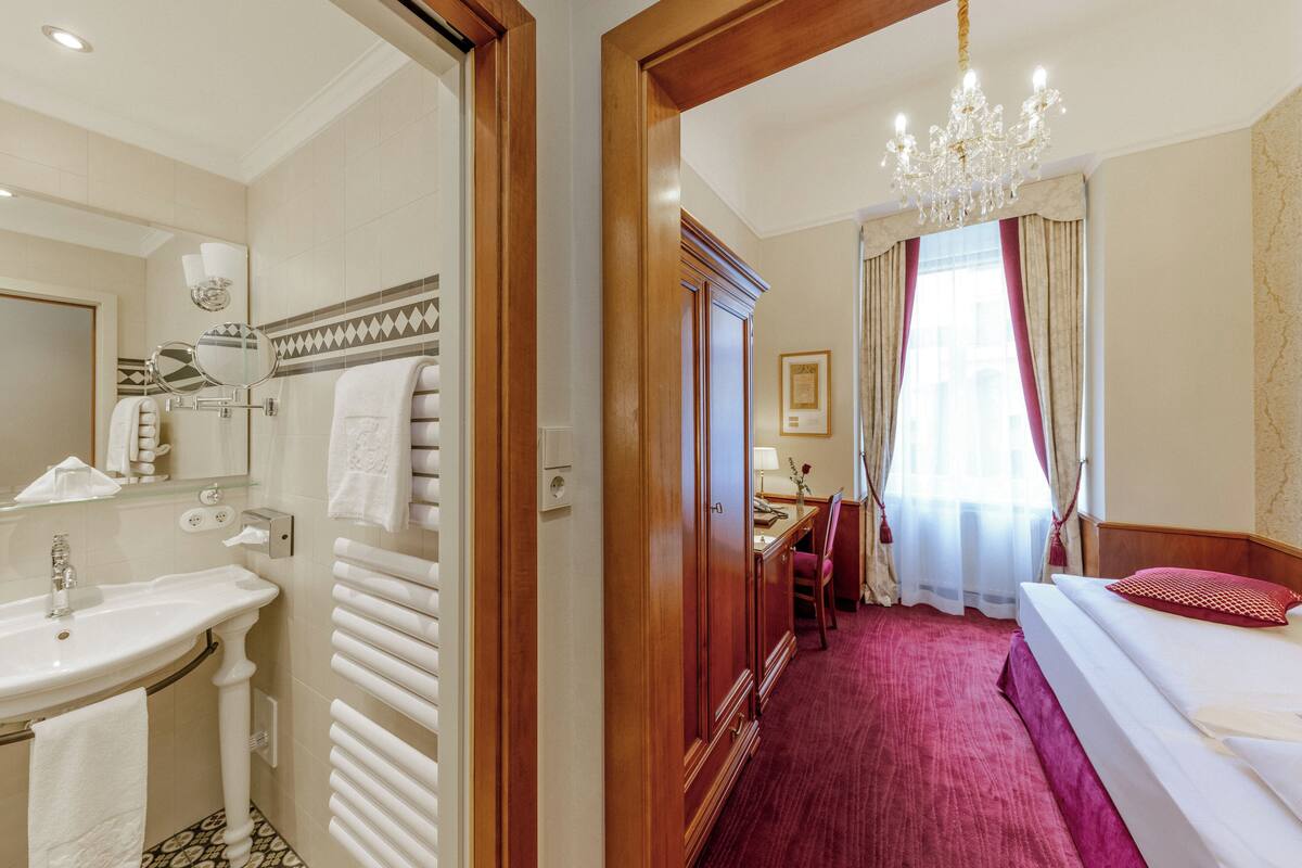 Een hotelkamer met een badkamer, een bed, een bureau en een kroonluchter.