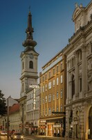 A historic building with a clock tower, Hotel Stefanie, and adjacent shops.