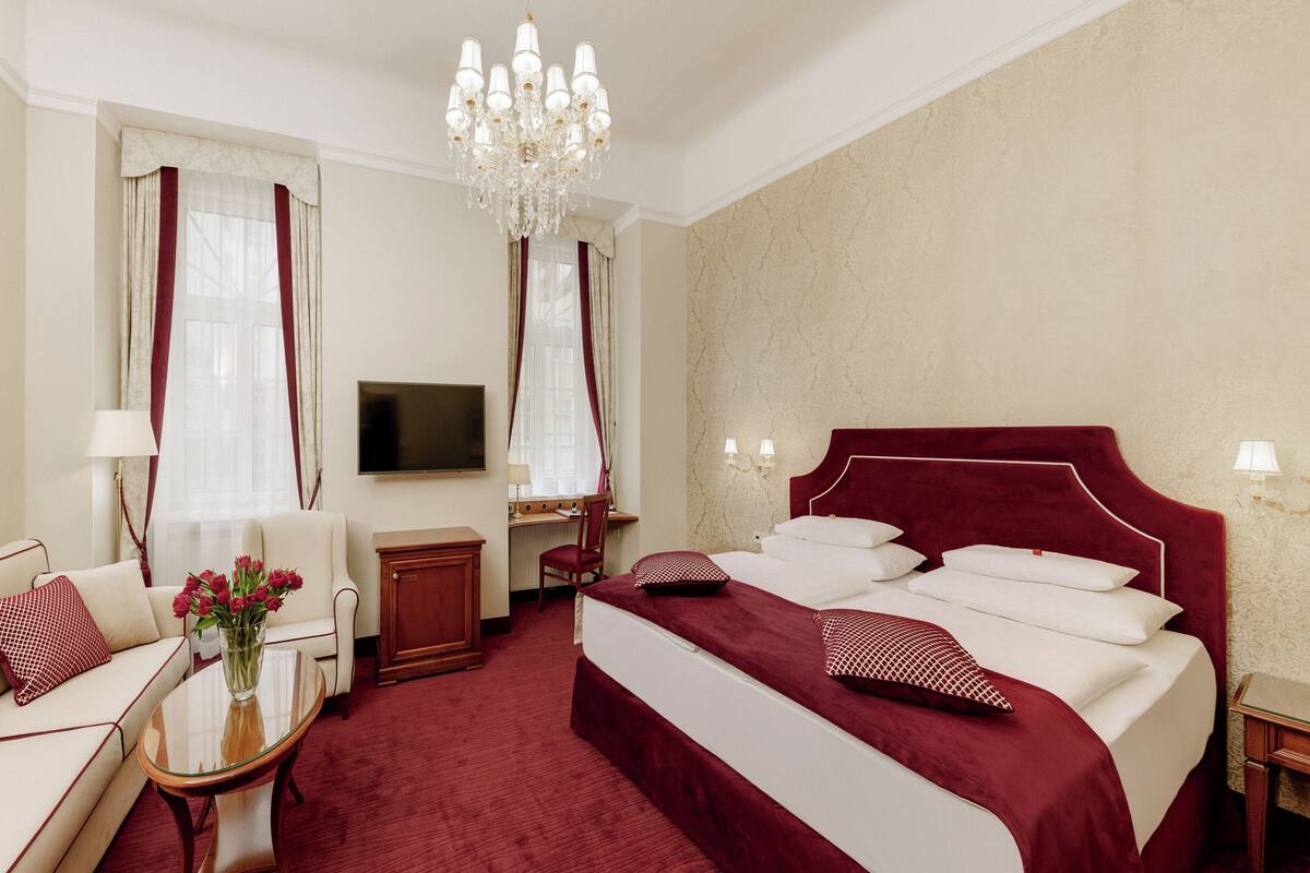 Een hotelkamer met een groot bed, een bureau, een stoel, een televisie en een kroonluchter.