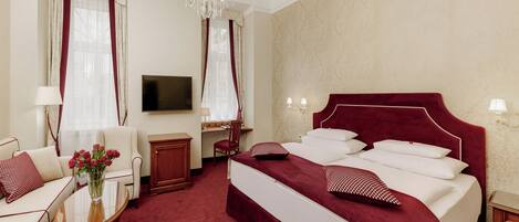 A hotel room with a large bed, a desk, a TV, and a chandelier.