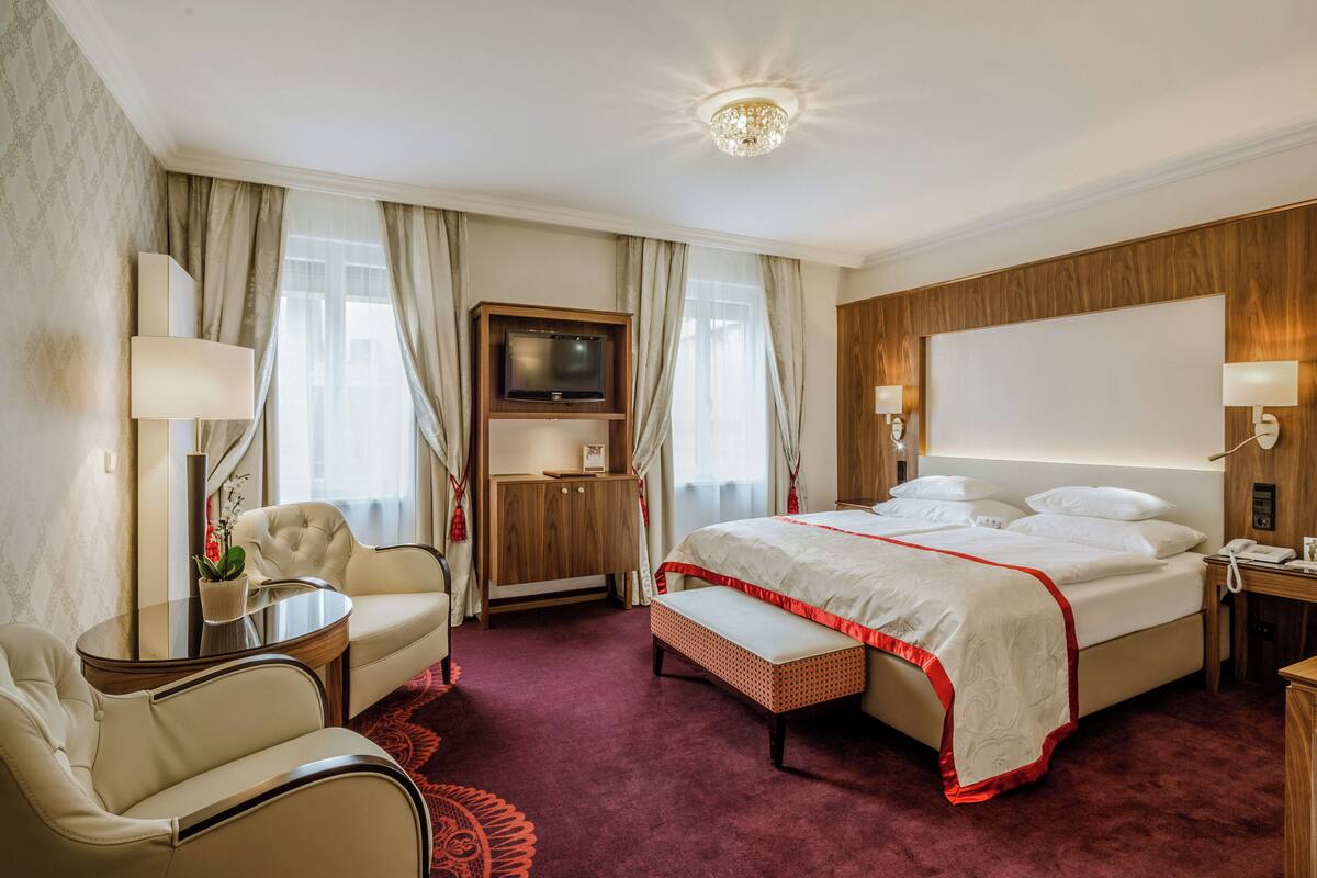Een hotelkamer met een groot bed, een bureau met stoel, een televisie en een groot raam met gordijnen.