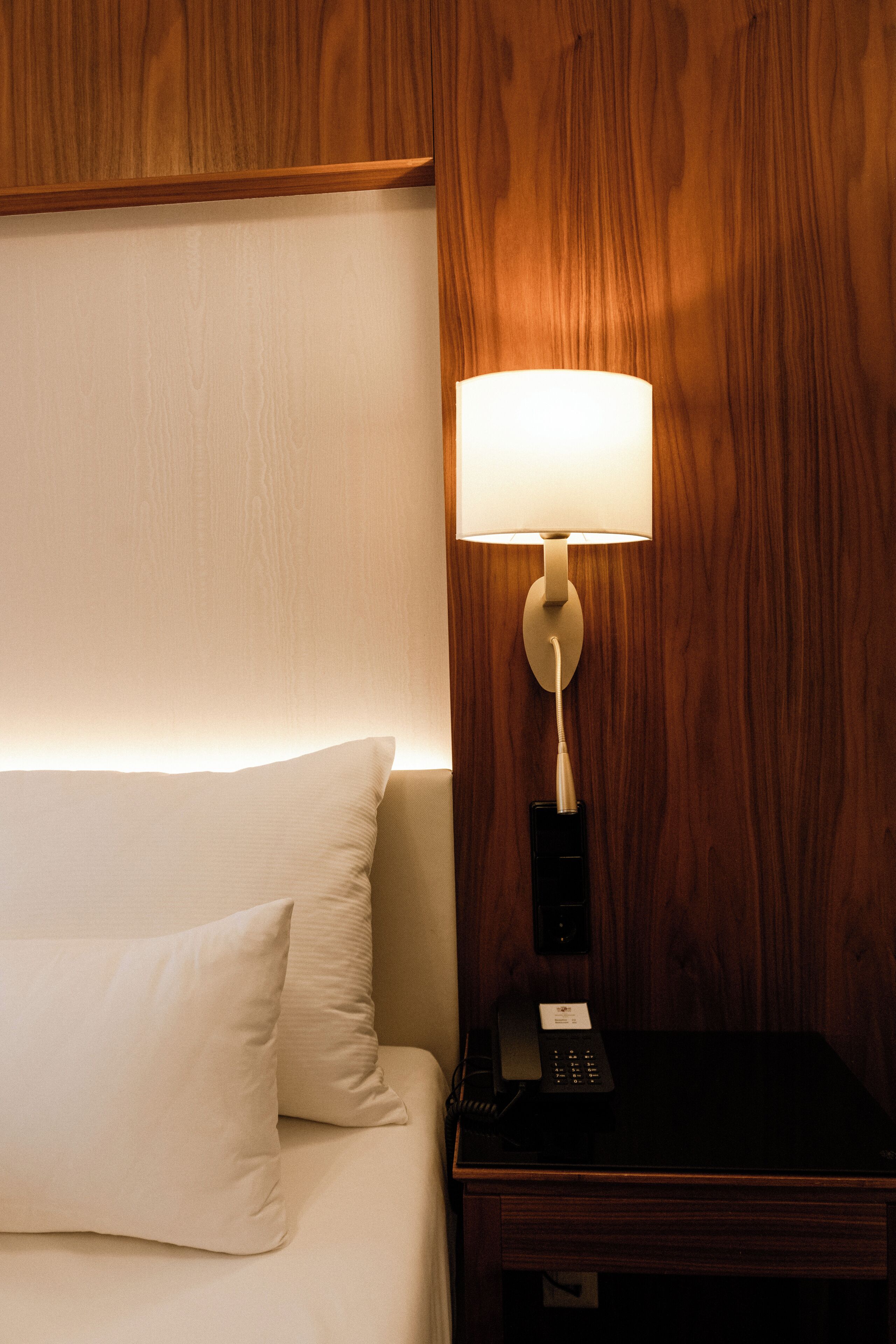 A hotel room with a bed, a nightstand, a lamp, and a telephone.