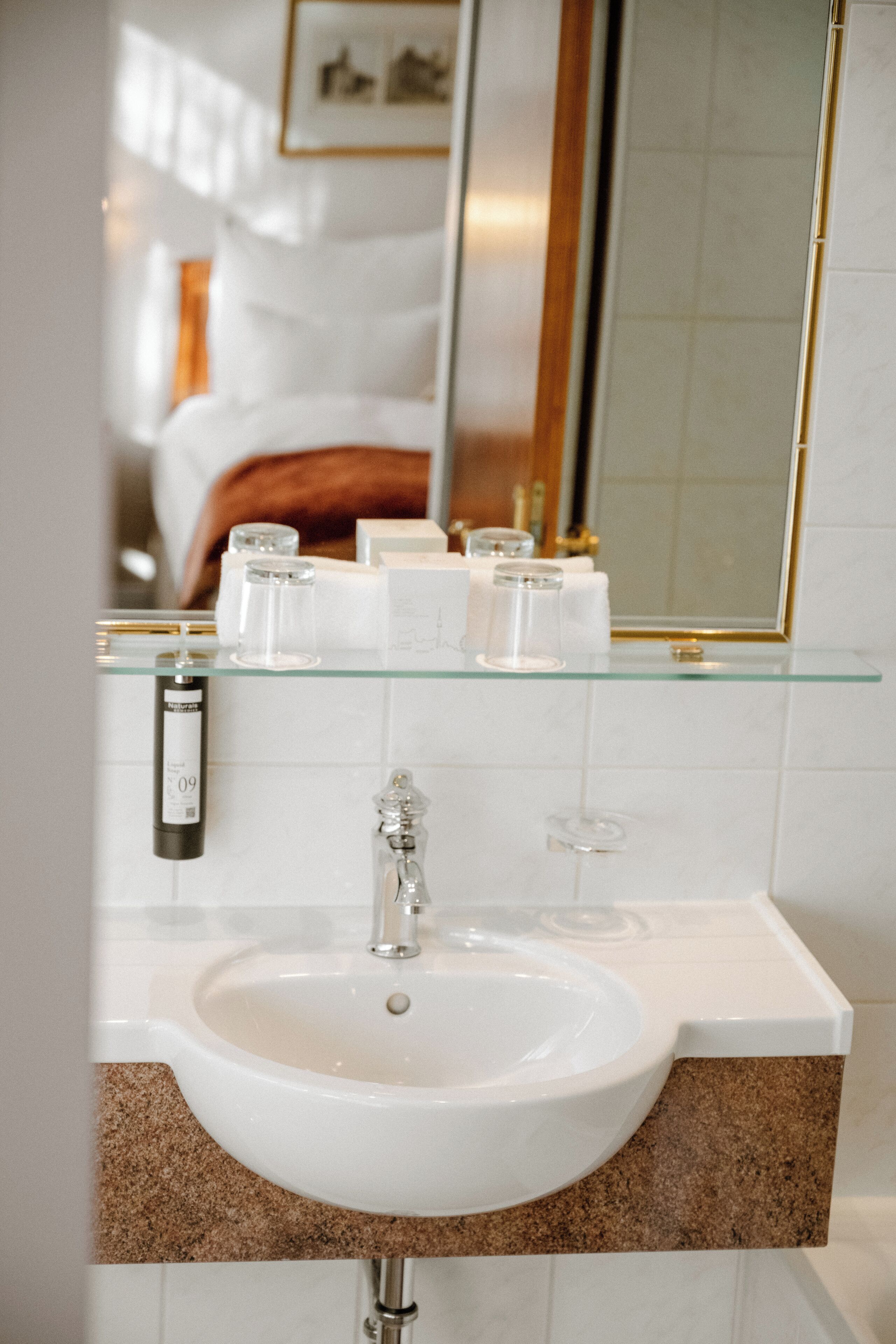 A bathroom with a white sink, glass shelf, and a mirror.