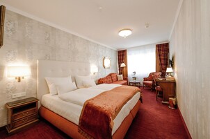 Quarto de hotel com uma cama grande, uma escrivaninha, uma cadeira e uma mesinha.