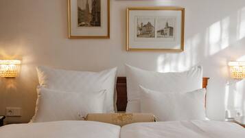 A neatly made bed with white linens and a decorative pillow, two wall-mounted lamps, and framed pictures on the wall.