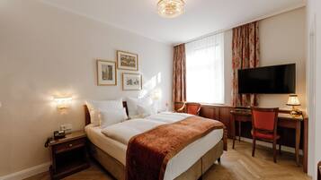 A hotel room with a bed, bedside table, lamp, desk, chair, TV, and curtains.