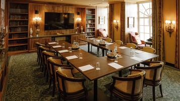 Une salle de conférence avec une longue table, des chaises, un téléviseur, des étagères et une grande fenêtre.