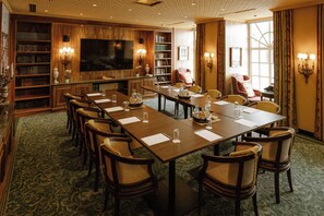 A conference room with a long table, chairs, a television, bookshelves, and a large window. - Hotel Stefanie (Vienna)