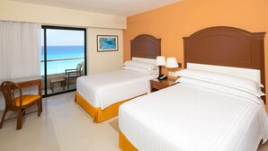 A hotel room with two beds, a desk, and a chair. There is a view of the ocean through a large window. - Occidental Tucancún All Inclusive (Cancun)