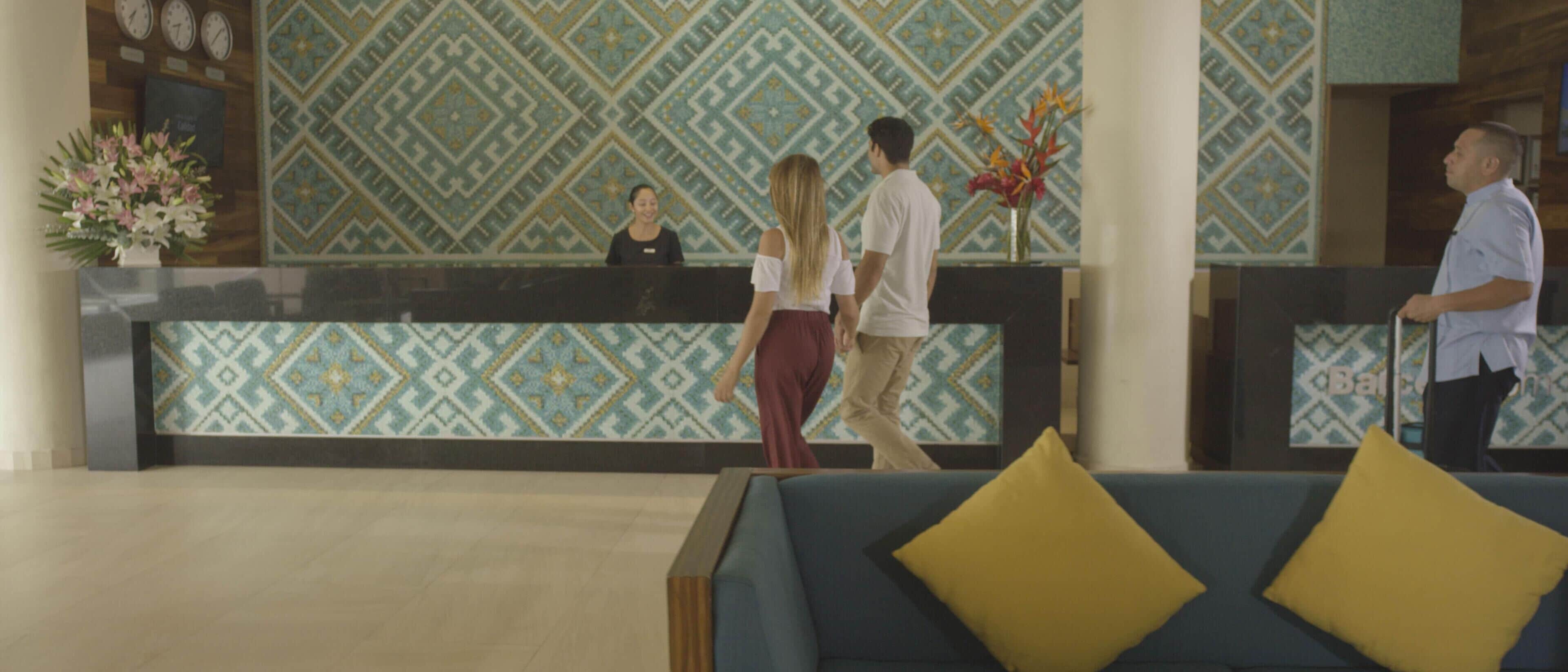 Een ontvangstgebied met een behang met patroon, een receptiebalie en een blauwe bank met gele kussens.