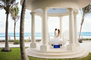 A gazebo with white columns, a table with a white tablecloth, and a view of the ocean. - Occidental Tucancún All Inclusive (Cancun)