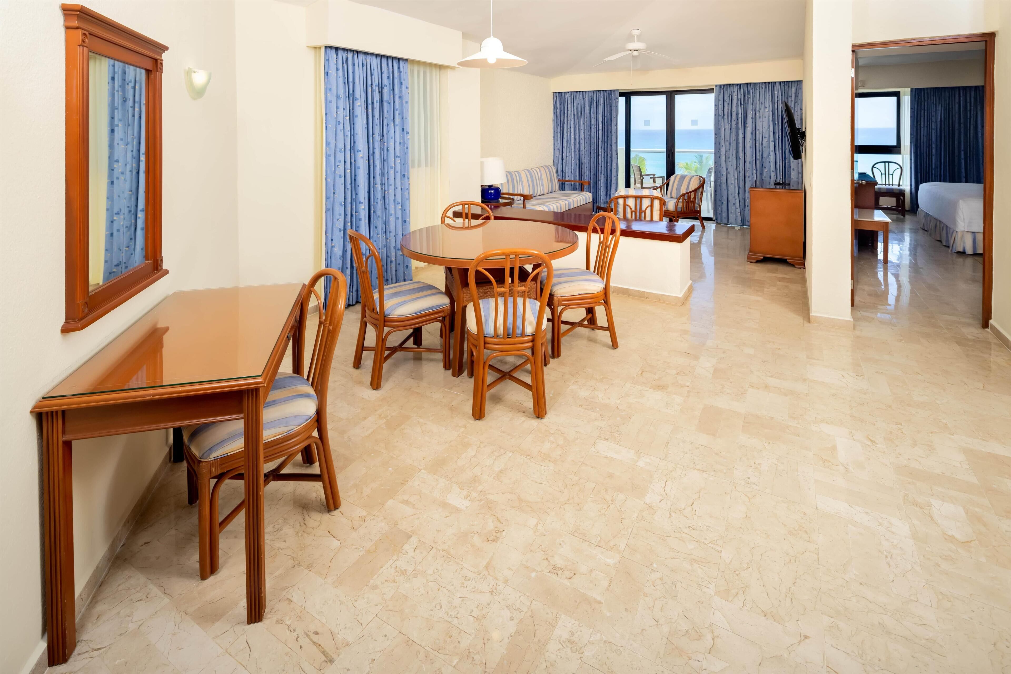 A hotel room with a dining area, a sofa, a bed, and a view of the sea.
