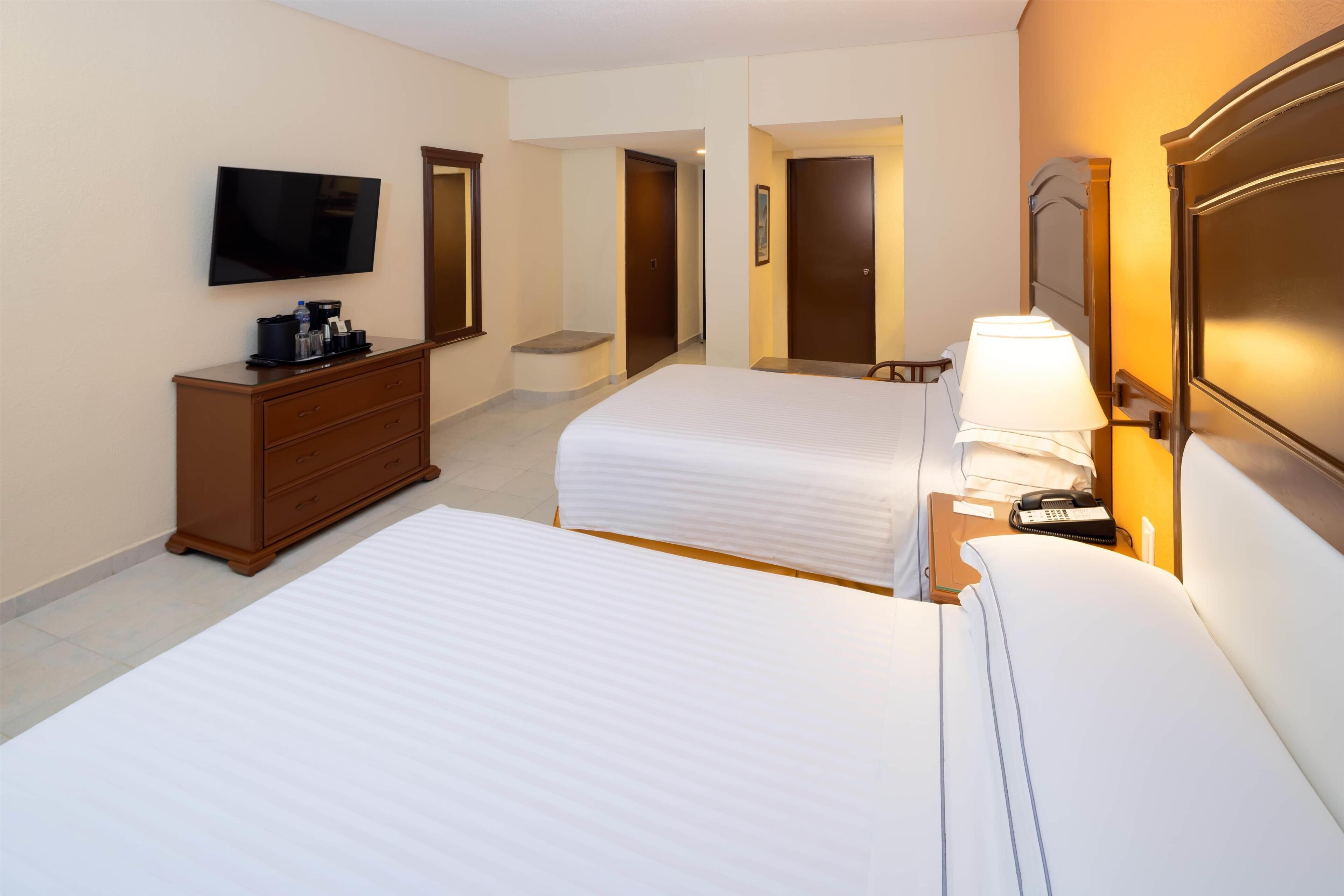 A hotel room with two beds, a TV, a dresser, and a lamp.