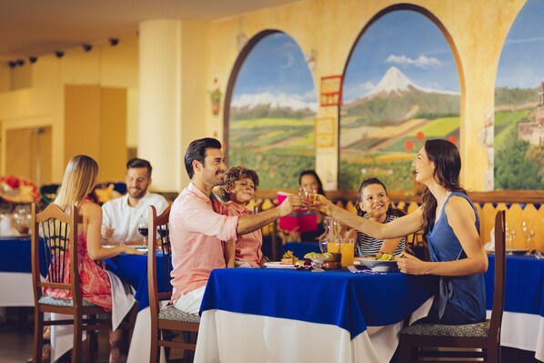 Un groupe de personnes est assis à une table dans un restaurant, et on peut voir, en arrière-plan, une fresque représentant un paysage de montagne.