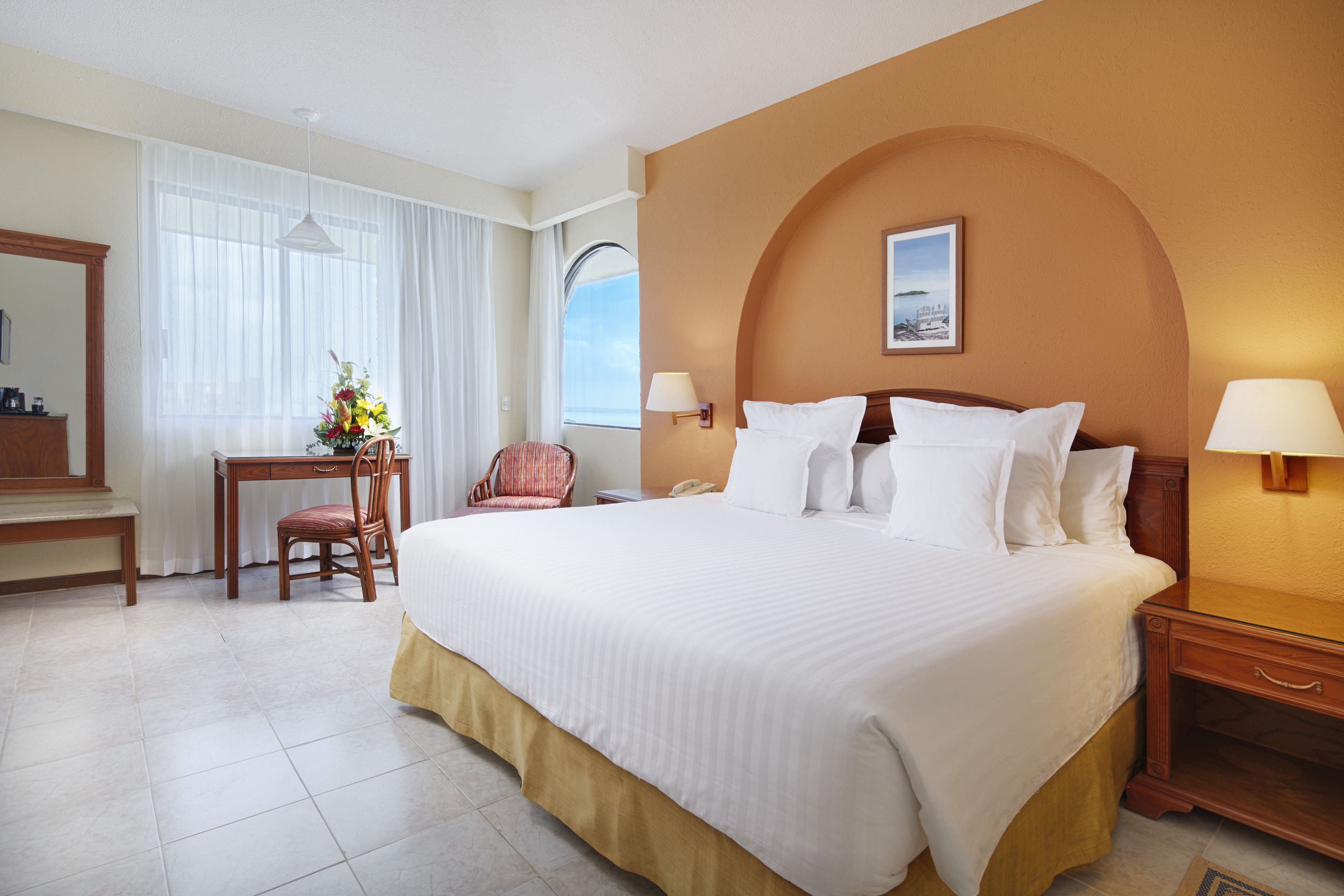 Une chambre d’hôtel avec un grand lit, un bureau avec une chaise, une lampe de bureau et une table de chevet avec une lampe.