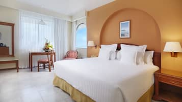 Une chambre d’hôtel avec un grand lit, un bureau avec une chaise, une lampe de bureau et une table de chevet avec une lampe.