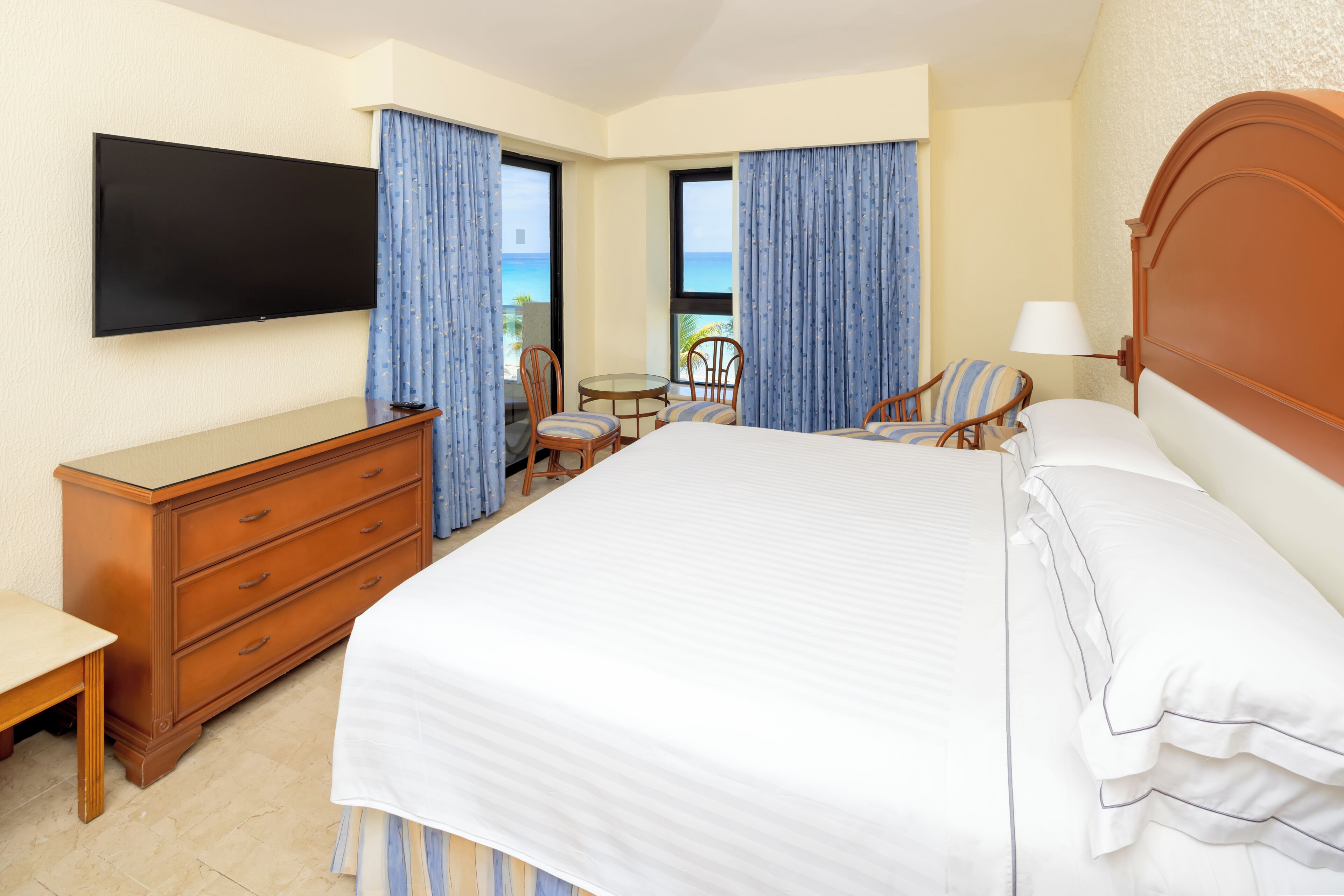 A hotel room with a bed, a TV, a desk, a chair, and a view of the ocean.