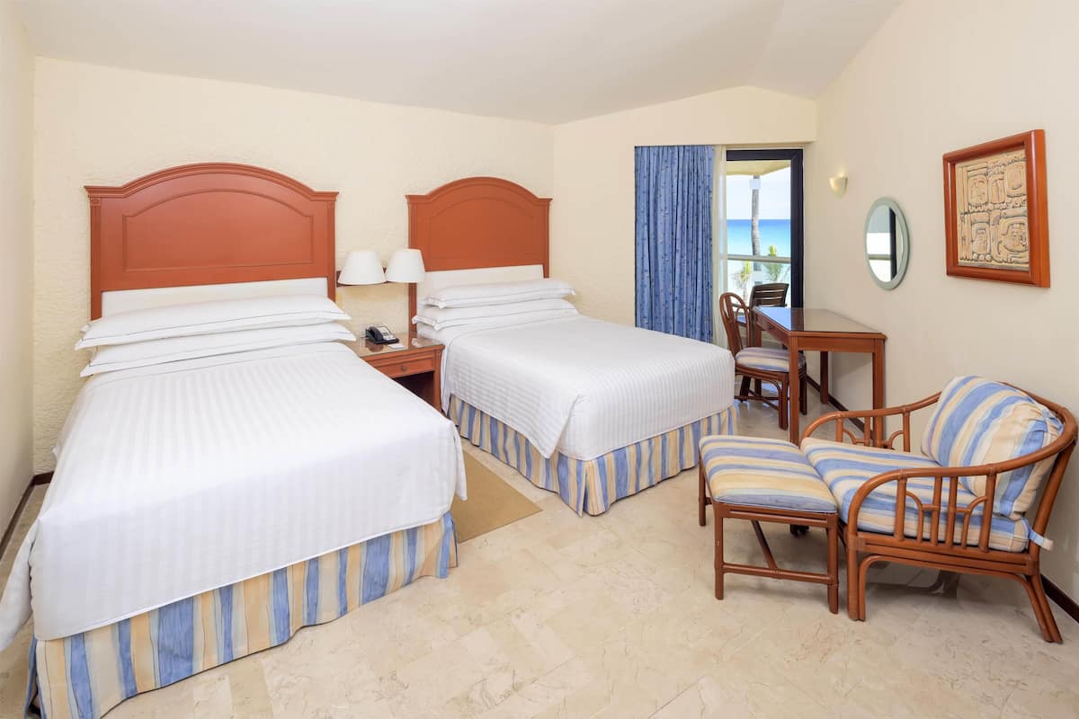 Une chambre d’hôtel avec deux lits, une chaise en bois, un bureau et une vue sur la mer.