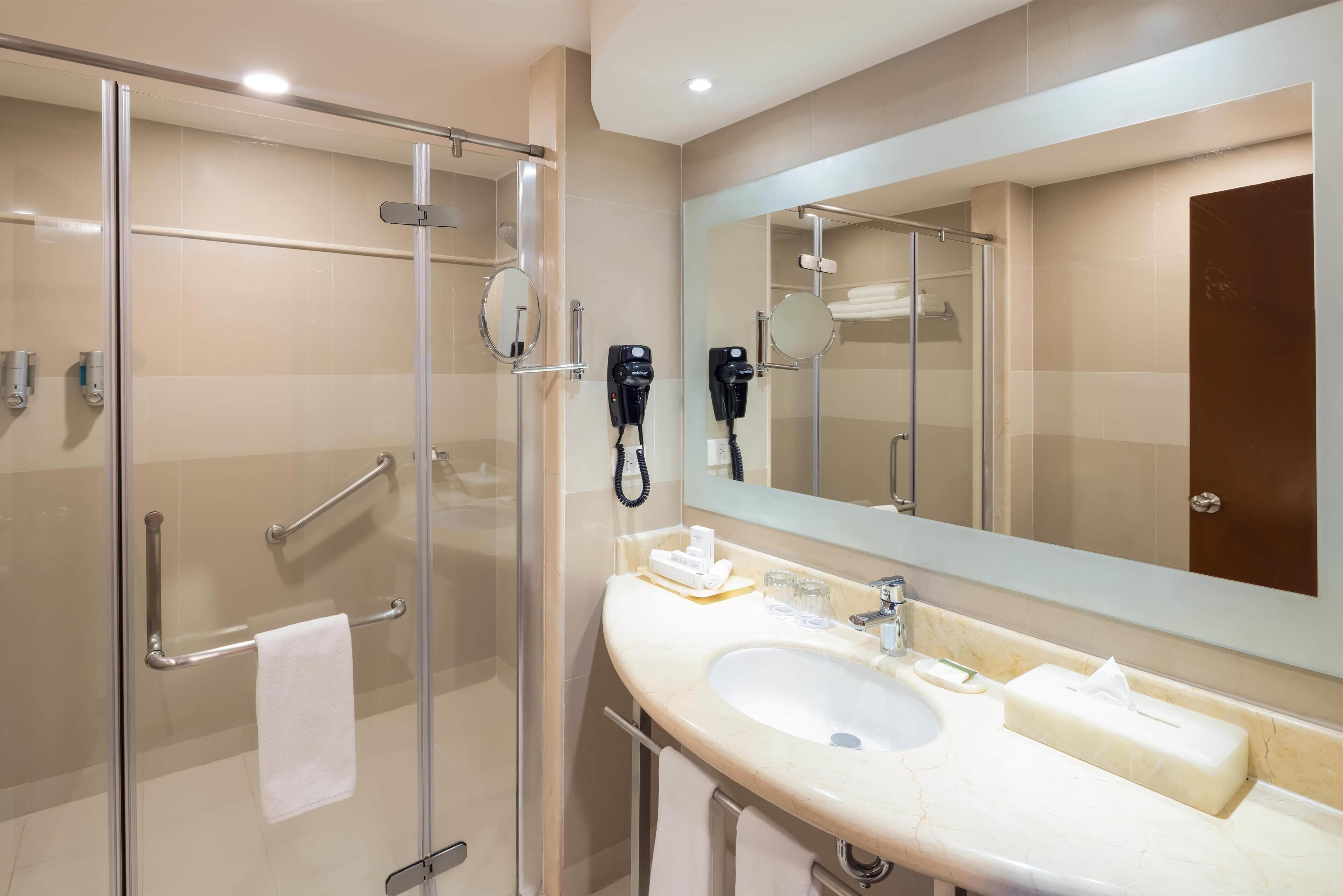 Un baño moderno con cabina de ducha de vidrio, lavamanos con espejo y secadores de pelo montados en la pared.
