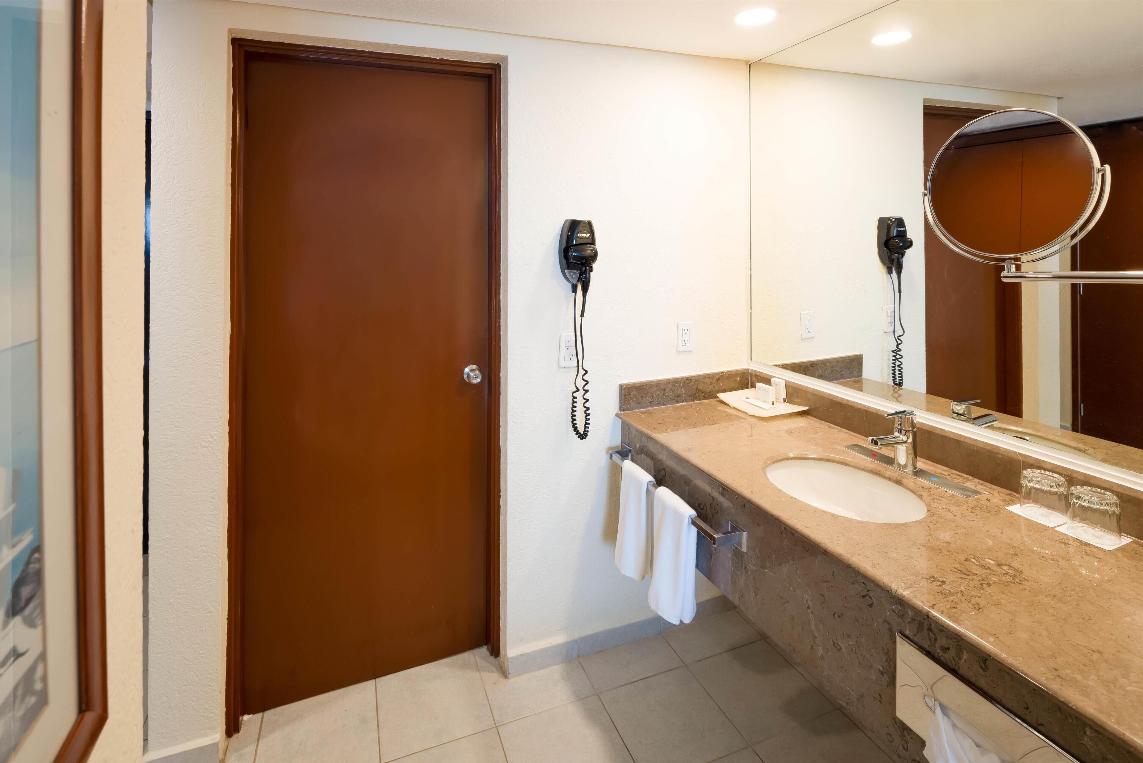 A bathroom with two sinks, a large mirror, and a hairdryer mounted on the wall.