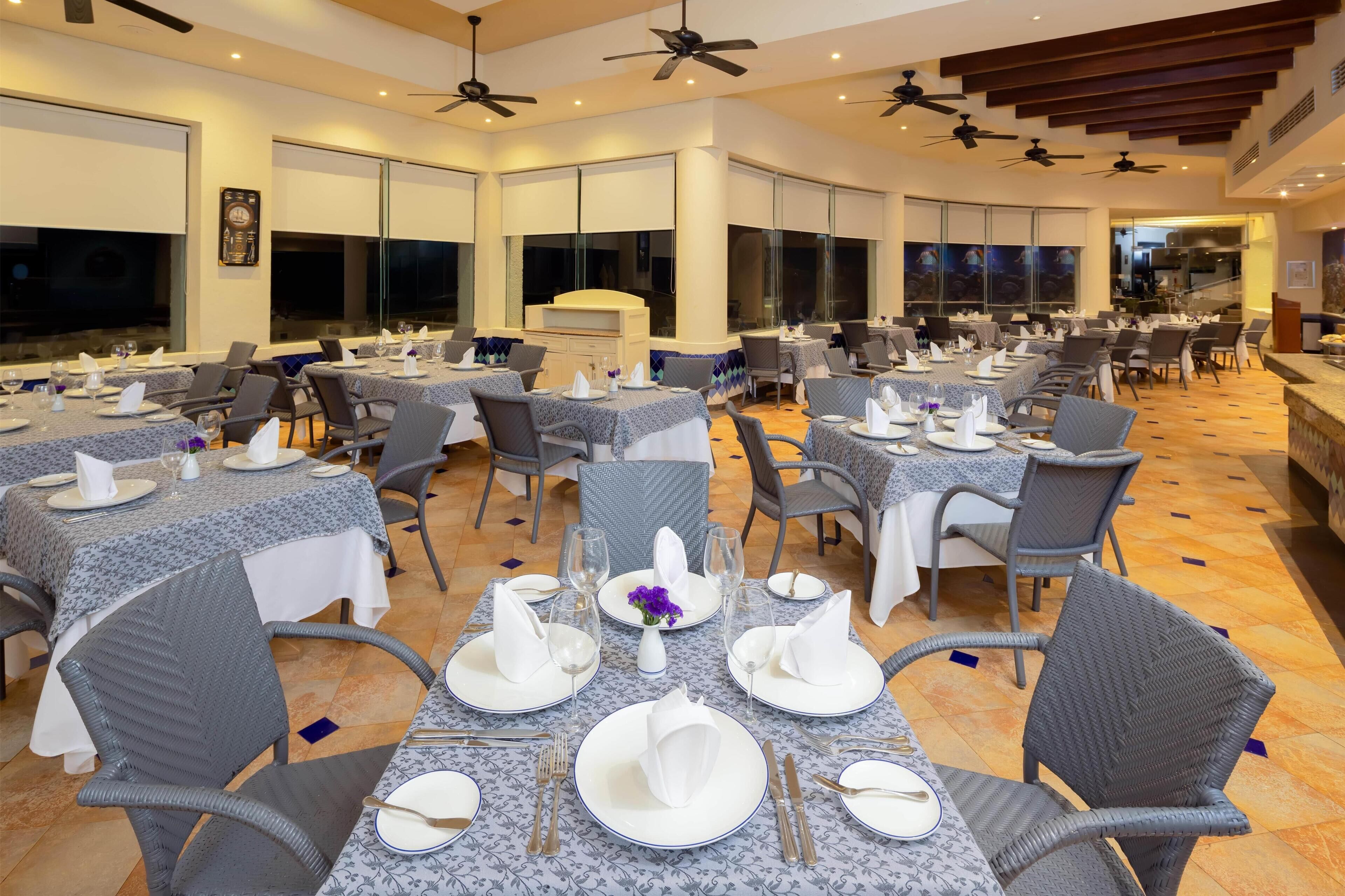 A spacious dining area with multiple tables set for guests, featuring grey chairs and white tablecloths.