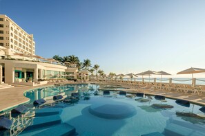 Un espace piscine aménagé dans un complexe hôtelier, avec des chaises longues, des parasols et un b âtiment à plusieurs étages.
