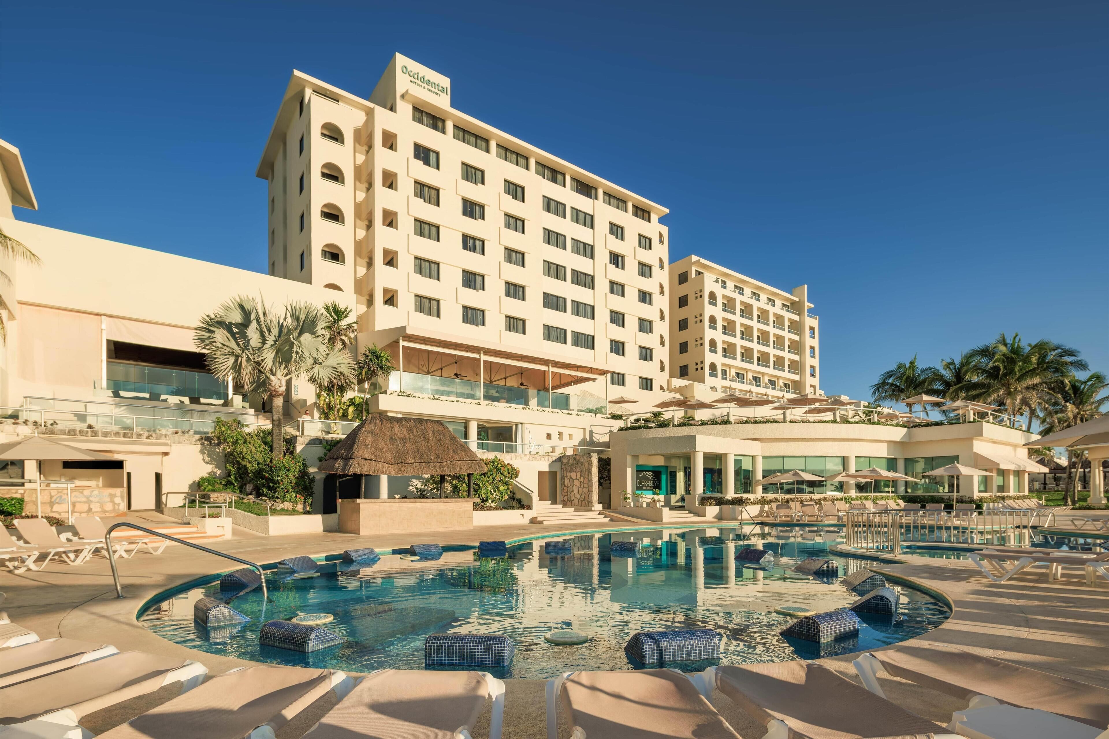 Um hotel com piscina, espreguiçadeiras e palmeiras.