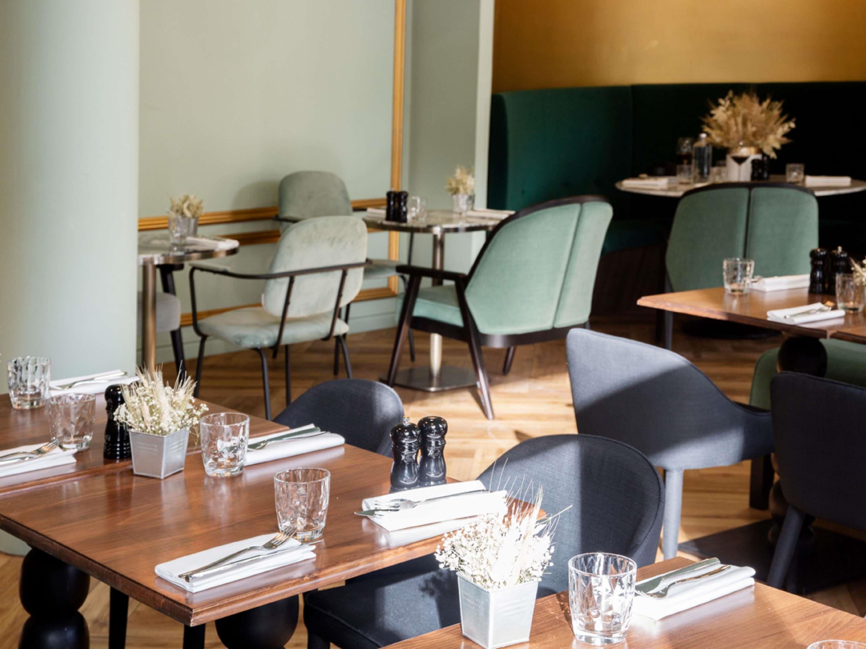 A restaurant interior with wooden tables, chairs, and a green accent wall.
