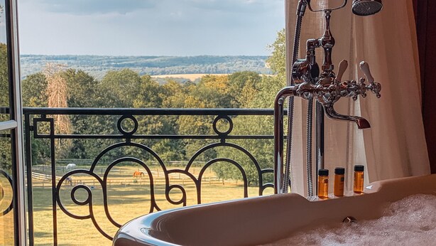 A bathroom with a bathtub, a window with a view of a green landscape, and a metal railing. - Demeures de campagne Domaine de Maffliers – Novotel (Maffliers)