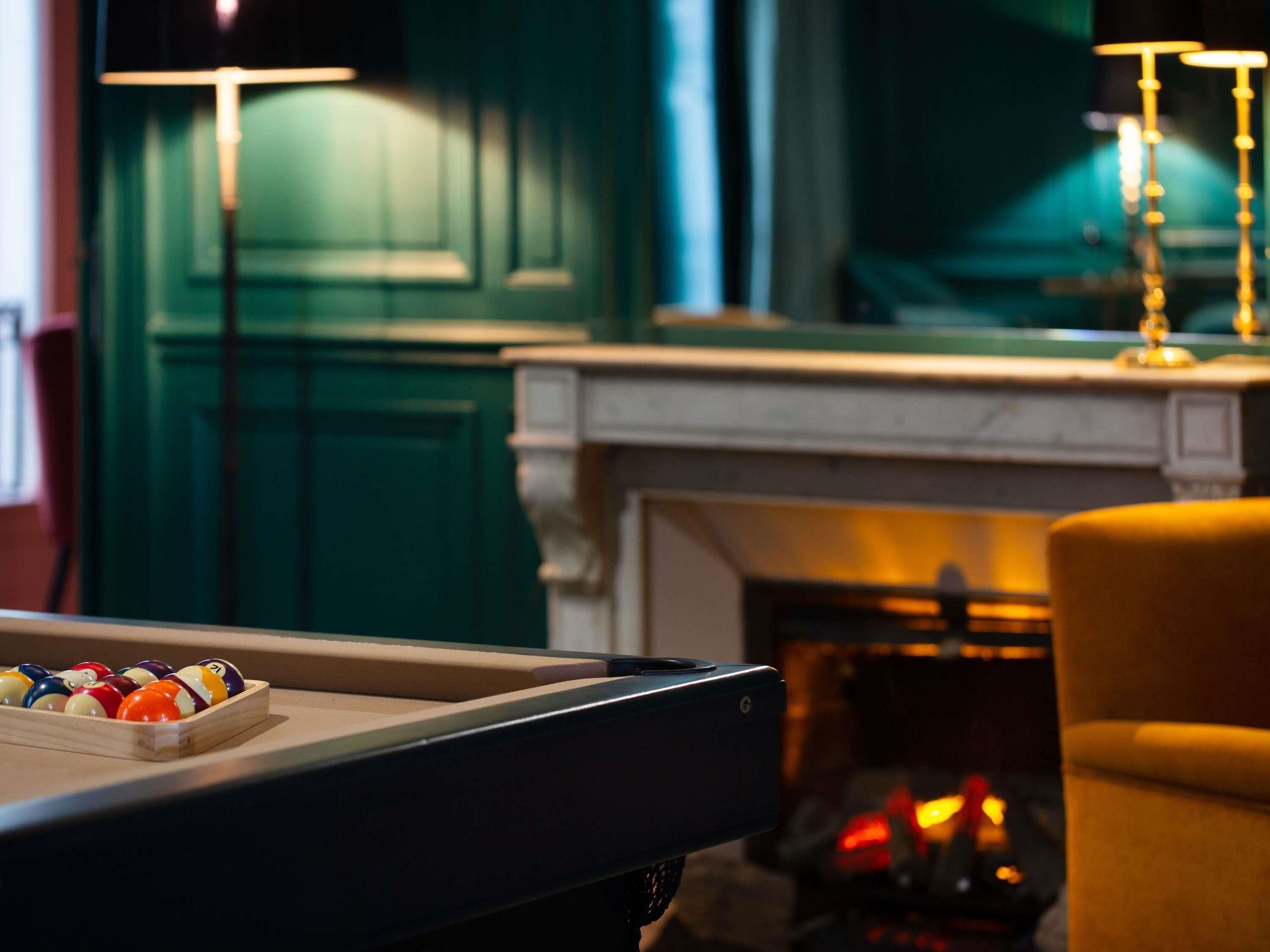 A billiards table with balls, a fireplace, and a green wall.