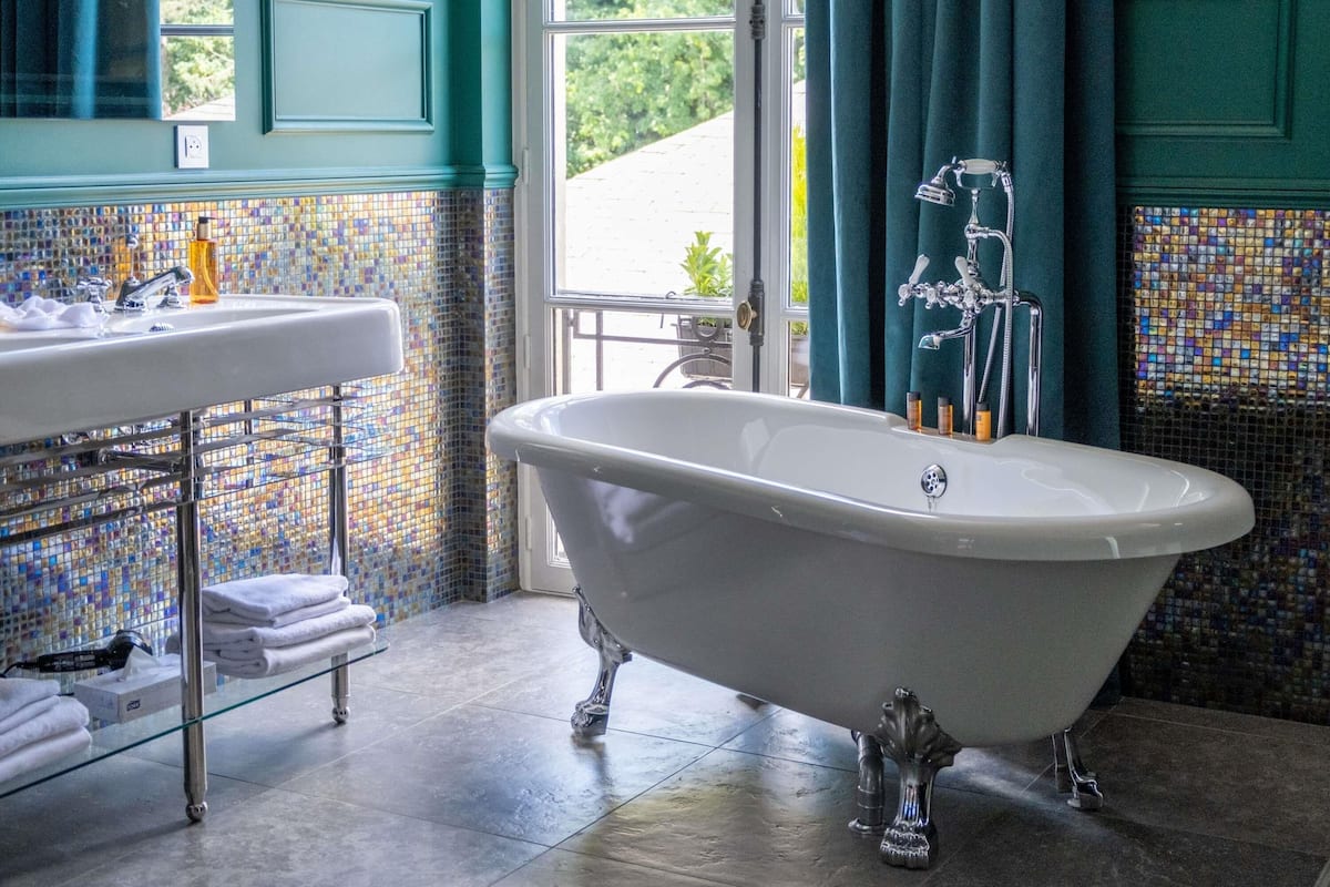 A bathroom with a freestanding bathtub, a sink with a mirror, and a window with curtains.