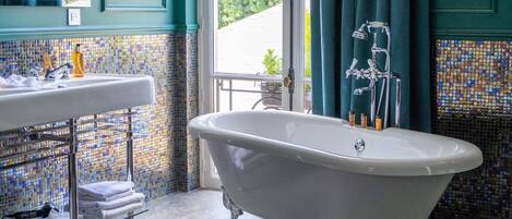 Un baño con una bañera independiente, un lavabo con espejo y una ventana con cortinas.