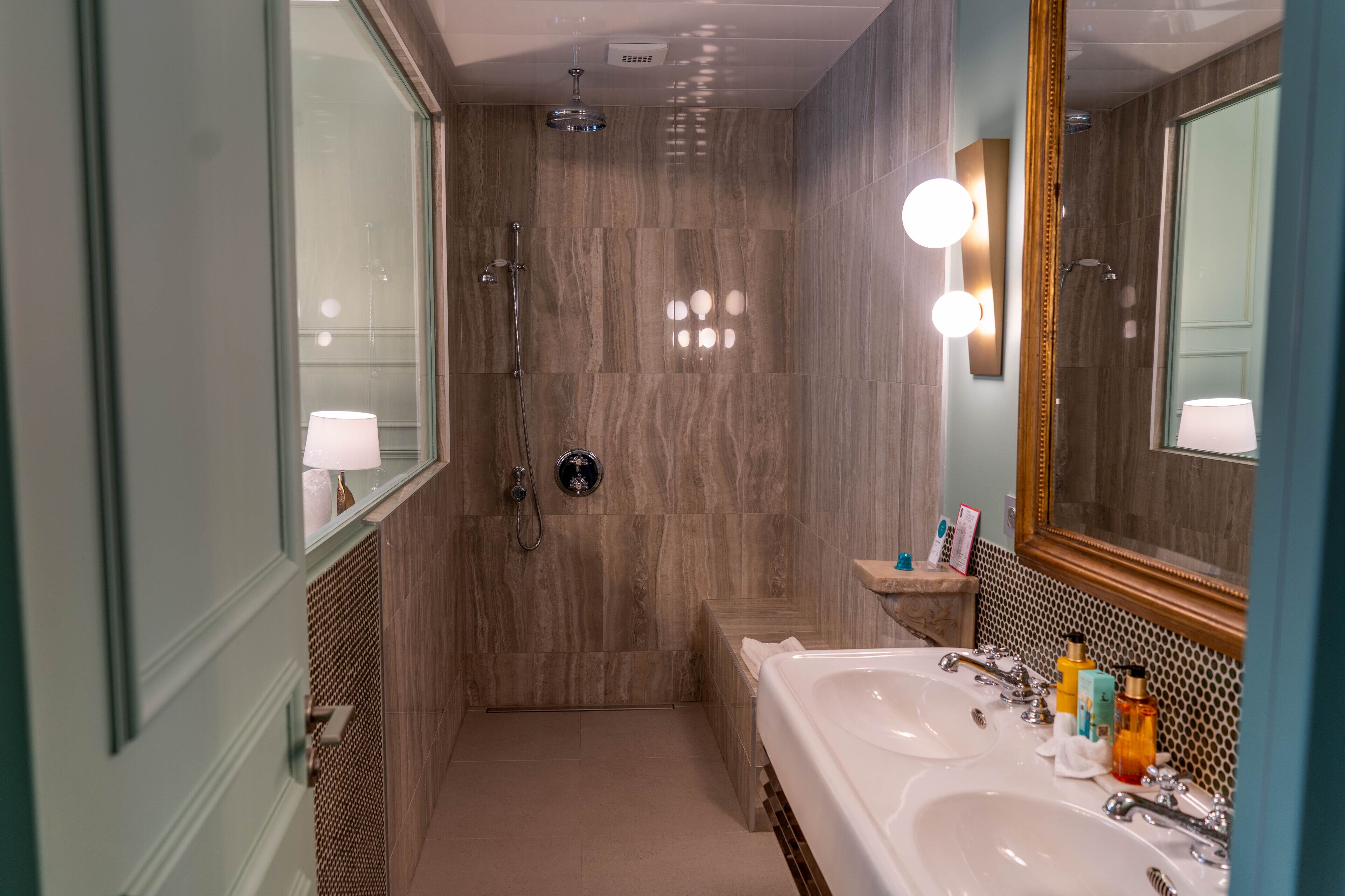 Une salle de bain moderne dotée d’un grand miroir, de deux lavabos, d’une douche et d’un meuble-lavabo avec des articles de toilette.