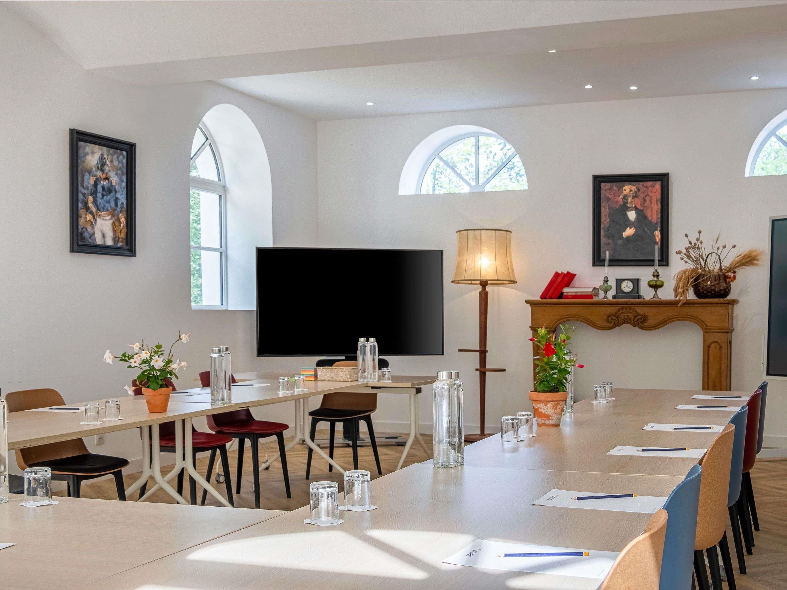 A conference room with a long table, chairs, a TV, a lamp, and a fireplace.