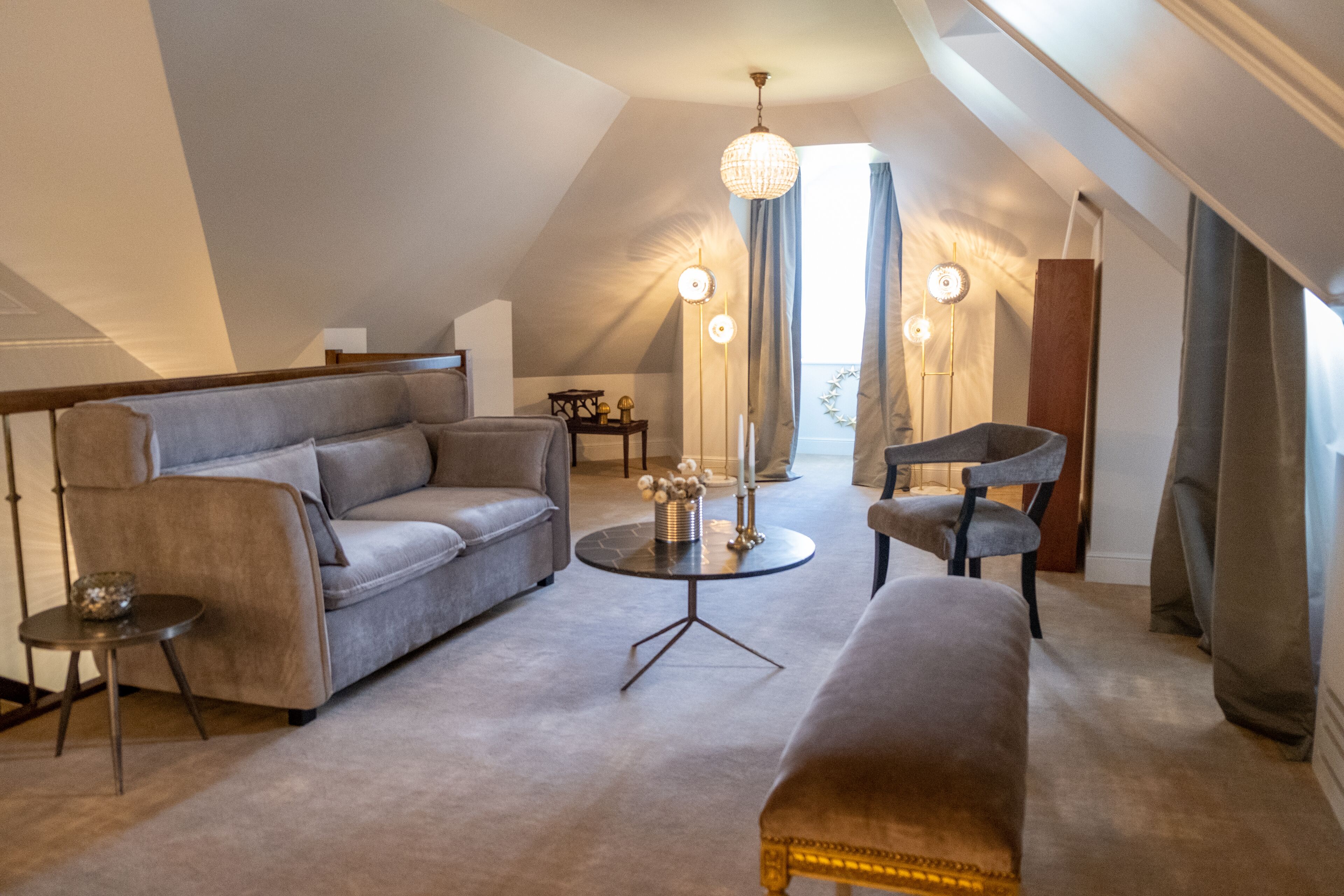 A modern loft bedroom with a sloped ceiling, a grey sofa, a round coffee table, and a bench.