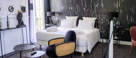 Una habitación de hotel moderna con una cama grande, una mesita pequeña, una silla y un adorno en la pared.