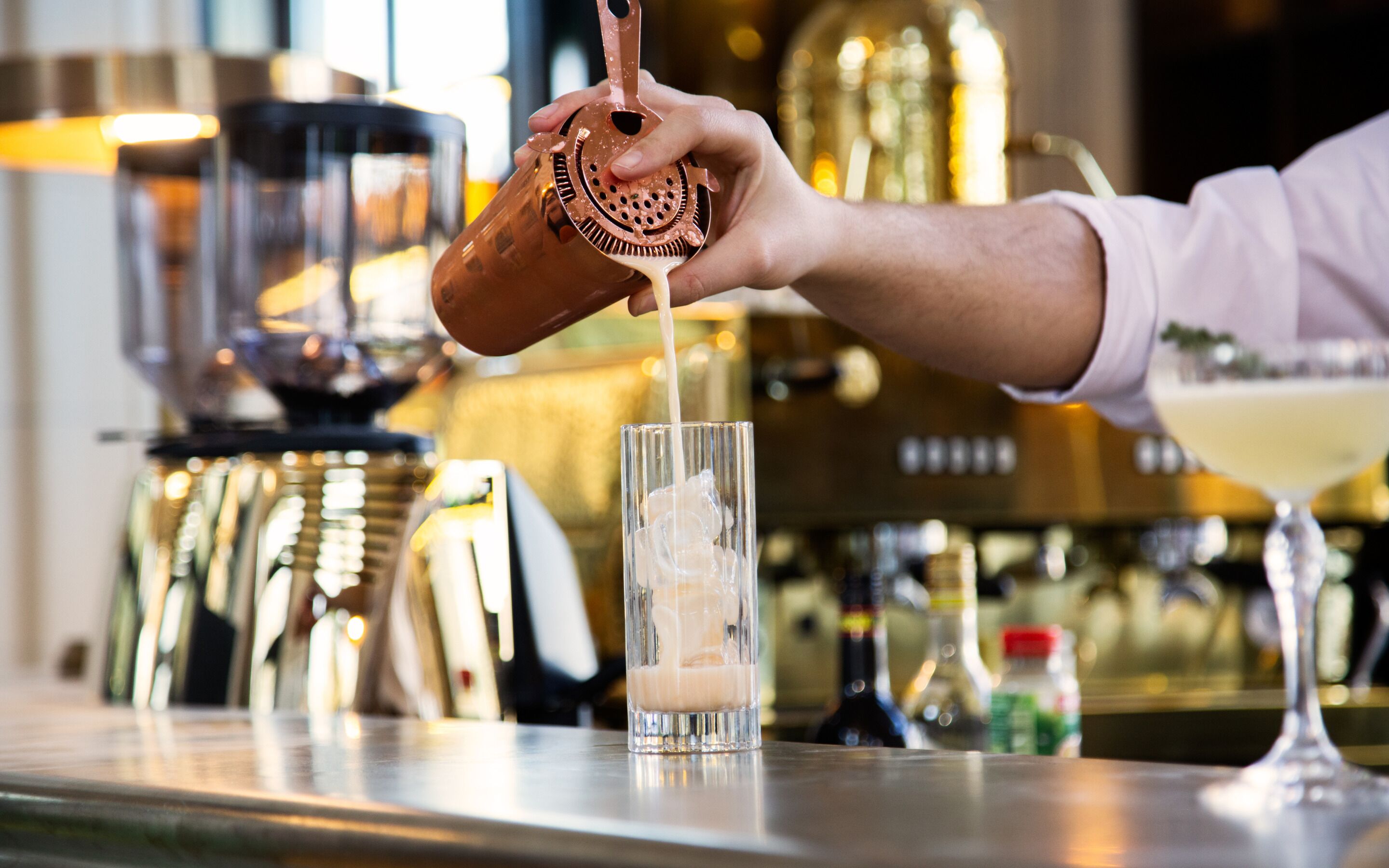 A bartender pouring a drink into a tall glass.