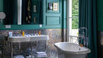 A bathroom with a freestanding bathtub, a sink with a mirror, and a tiled wall.