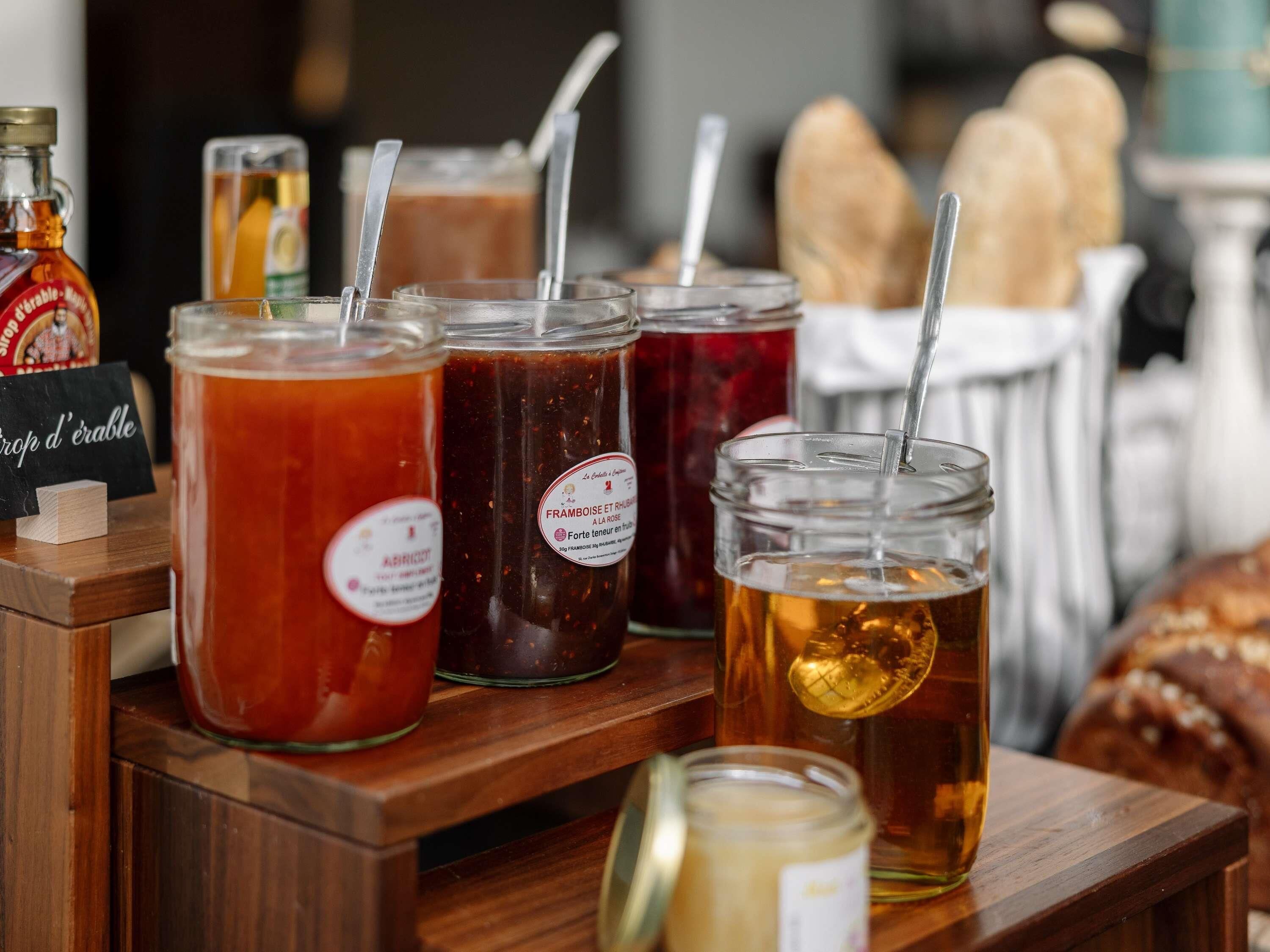 A wooden display with various jars of preserves and a bottle of syrup.