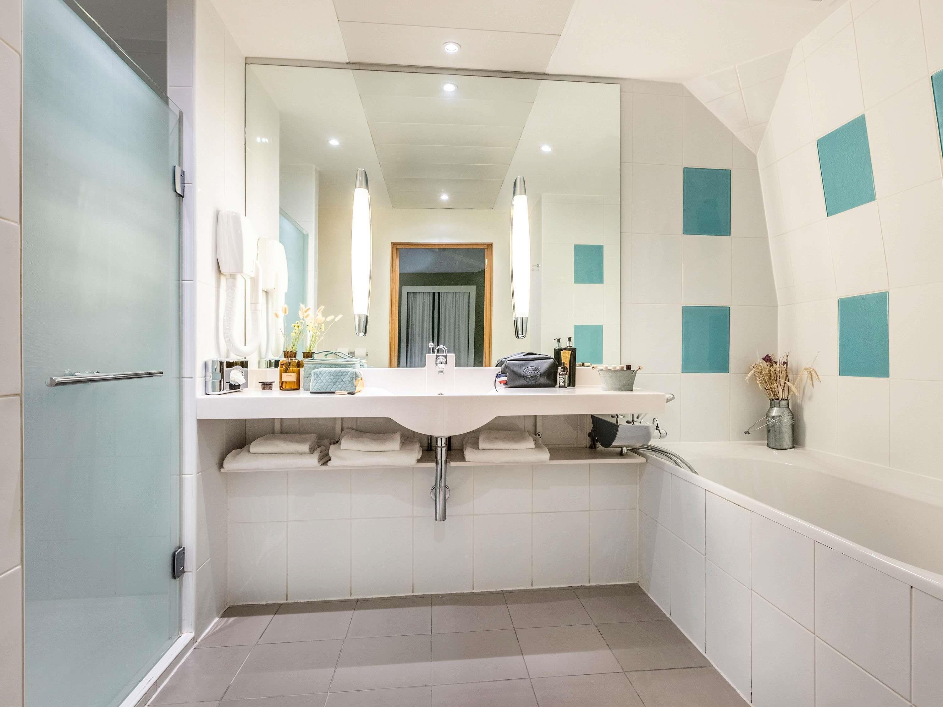 A modern bathroom with a large mirror, two sinks, a shower, and a towel rack.