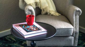 A small round table with a book and a red mug, a grey armchair with a beige throw blanket, and a patterned carpet.
